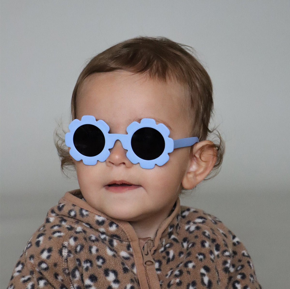 Paire de lunettes de soleil bébé catégorie 4, monture en TPEE bleue en forme de fleur. Mise en situation portée de profil