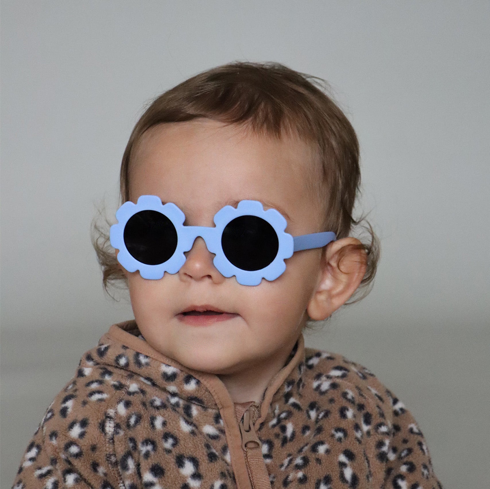 Paire de lunettes de soleil bébé catégorie 4, monture en TPEE bleue en forme de fleur. Mise en situation portée de profil